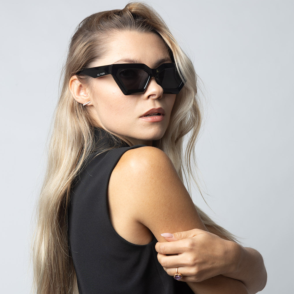 Woman wearing black sunglasses and a black sleeveless top against a light gray background