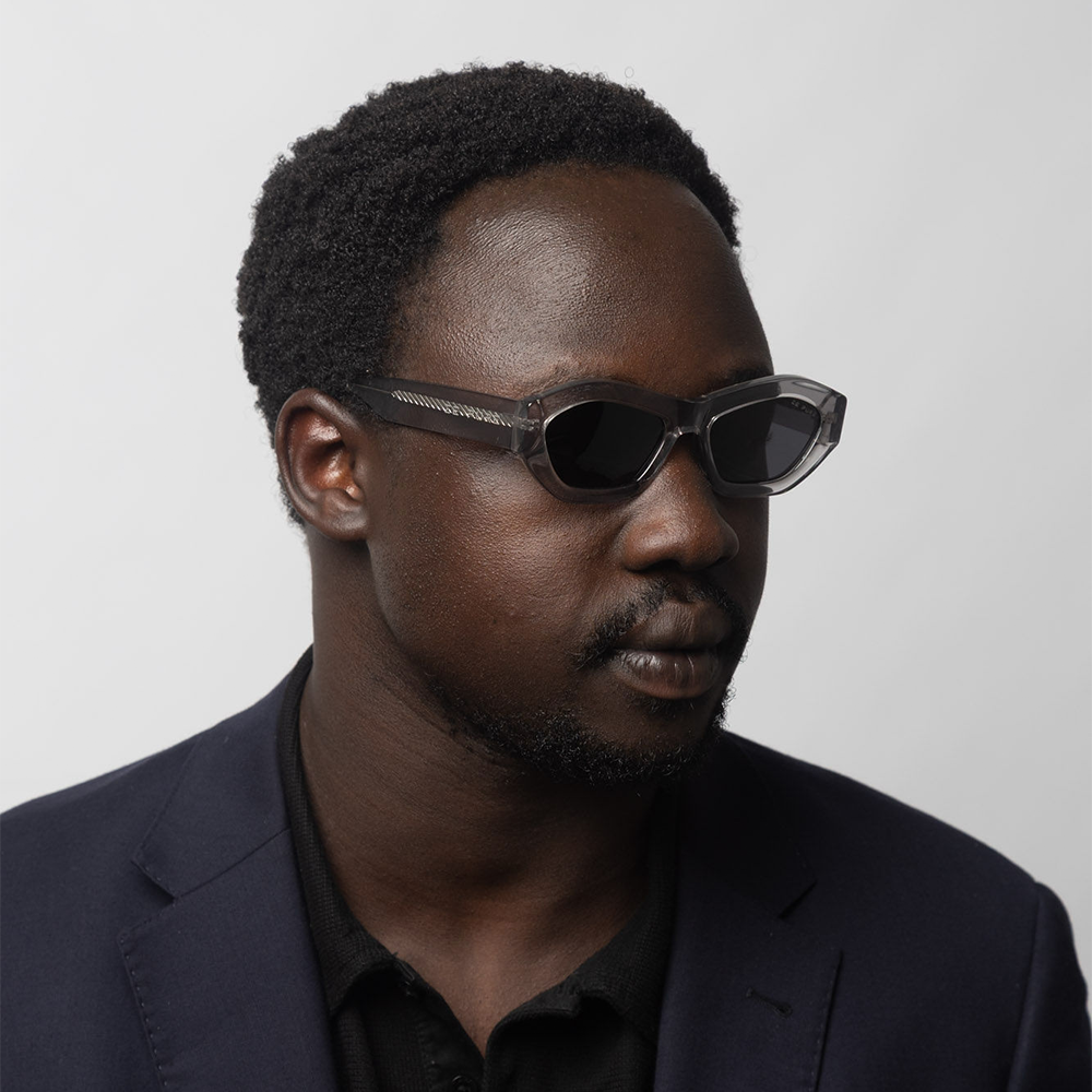 Man wearing sunglasses and a dark suit against a plain background