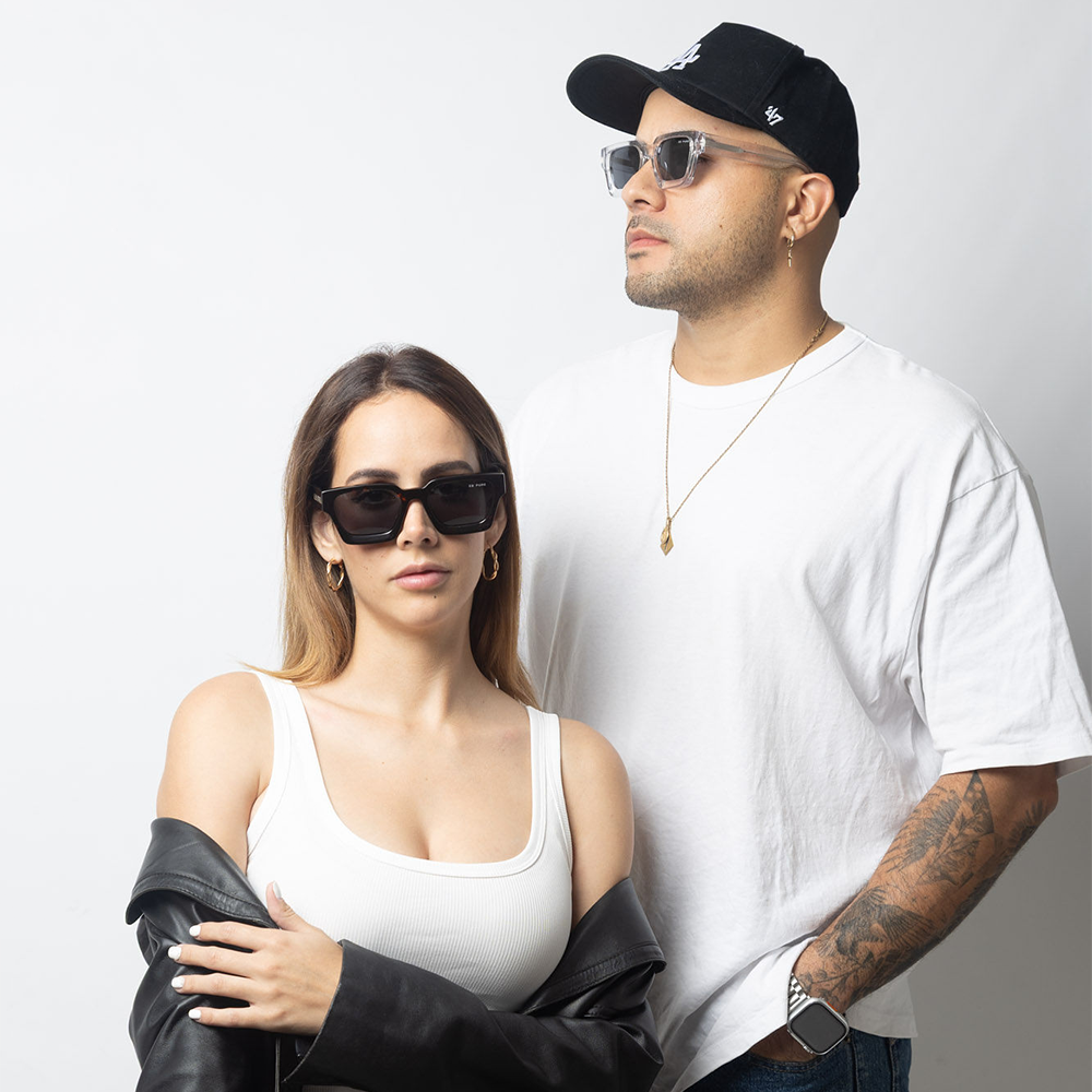 Two people wearing sunglasses and casual clothing against a plain background