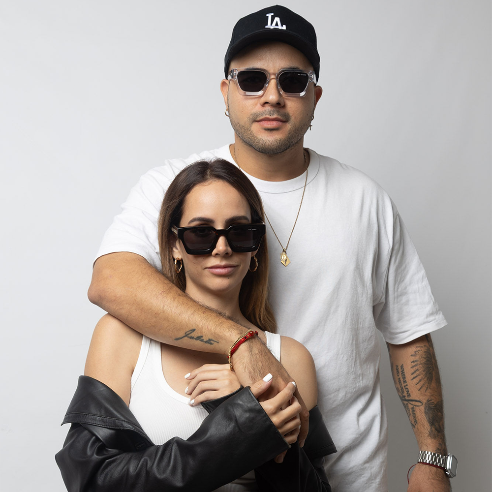 Two people embracing, one wearing a white t-shirt and black cap, the other in a white top and black jacket.