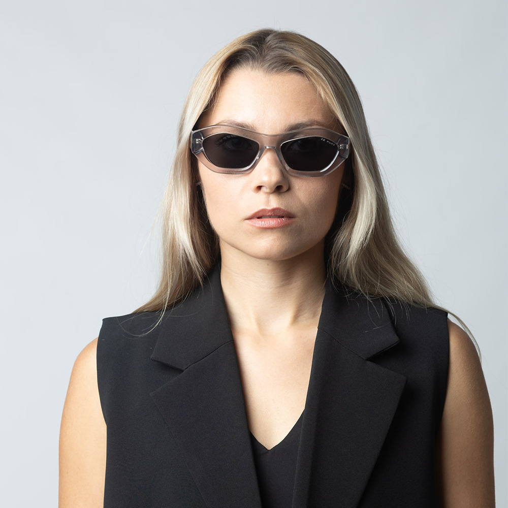 Woman wearing a black sleeveless blazer and sunglasses against a gray background