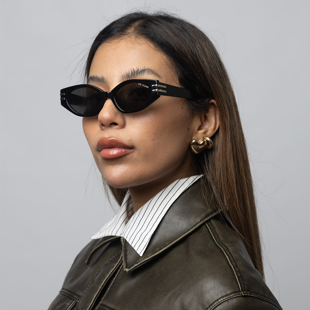 Woman wearing black sunglasses and a brown leather jacket against a gray background