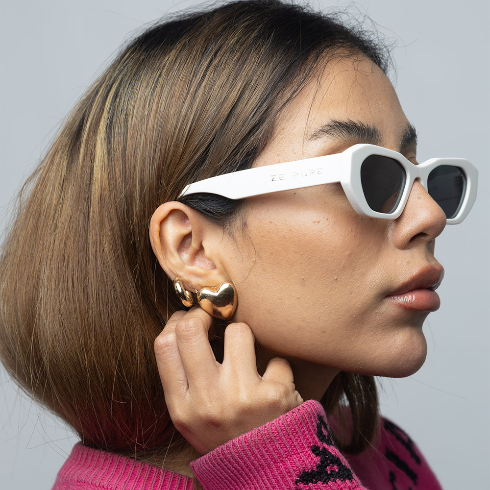 Woman wearing white sunglasses and gold earrings, with a neutral background