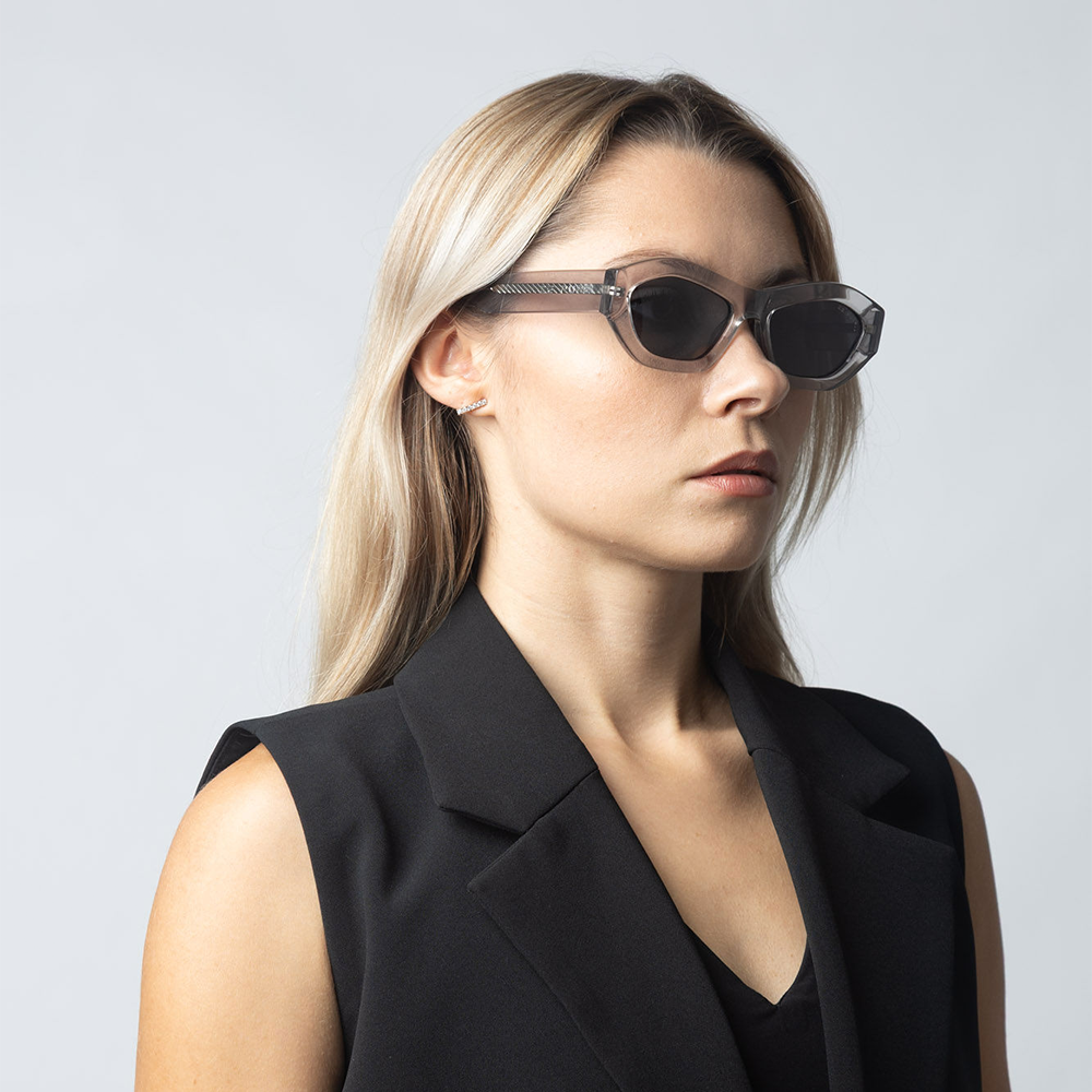 Woman wearing black sunglasses and a black outfit against a light gray background