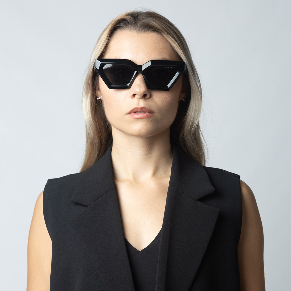 Woman wearing black sunglasses and a black outfit against a light gray background