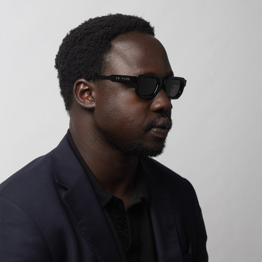 Man wearing dark sunglasses and a dark jacket against a plain background