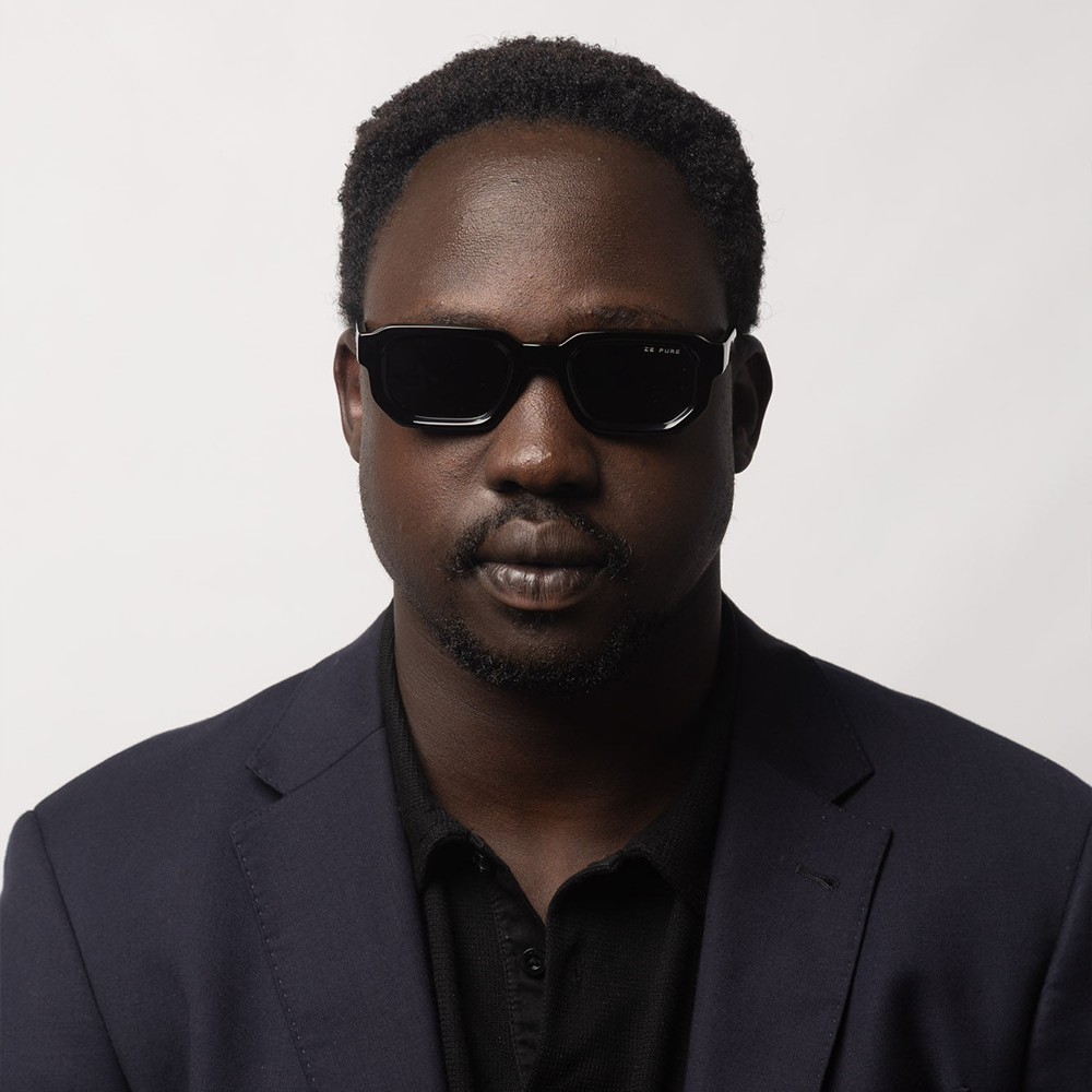 Man wearing dark sunglasses and a dark suit against a light background
