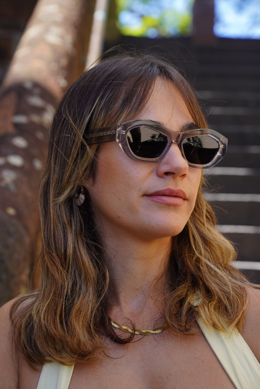 A close-up shot of a woman with wavy hair, wearing a cream dress and Zepure's Sunny Confidence sunglasses.