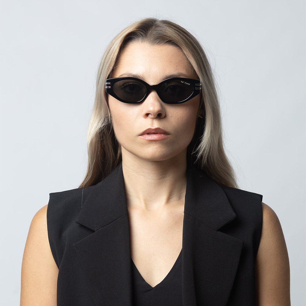 Woman wearing black sunglasses and a black sleeveless top against a light gray background