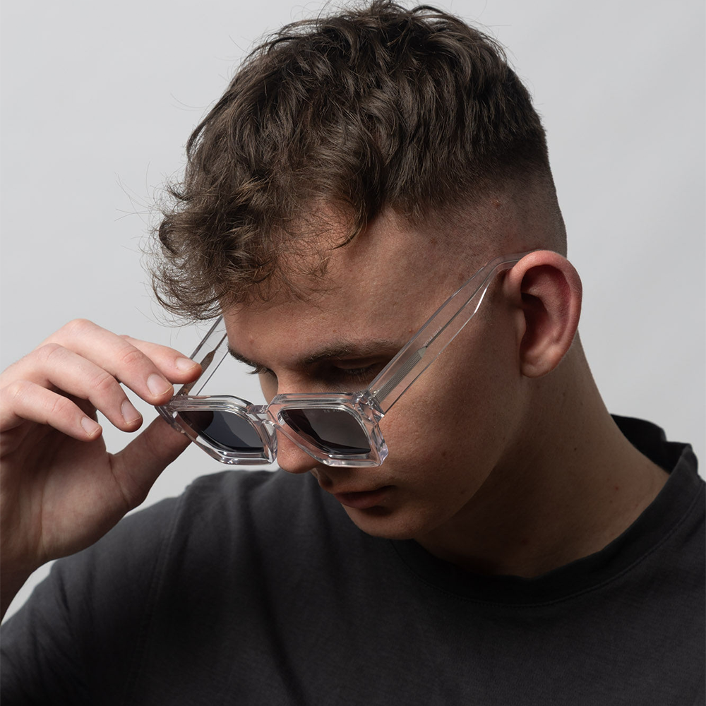 Person wearing hexagonal sunglasses with a neutral background