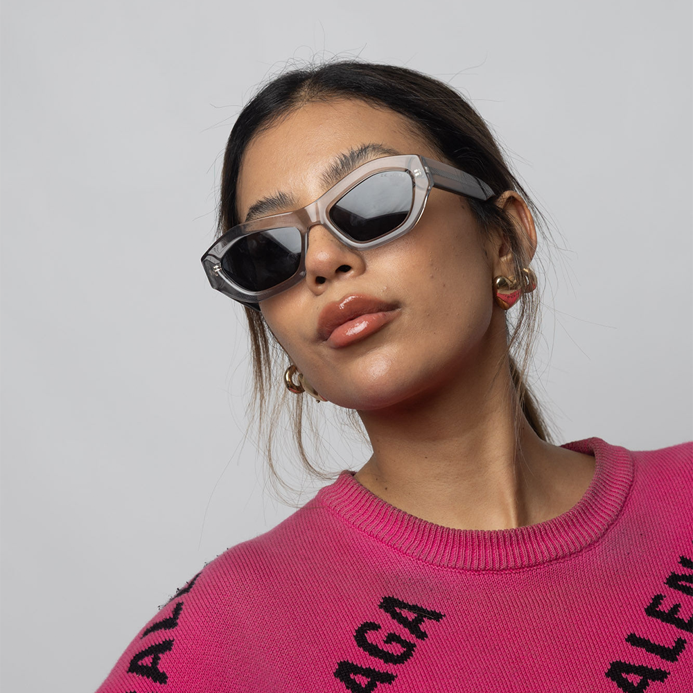 Person wearing a pink sweater with text and sunglasses on a plain background