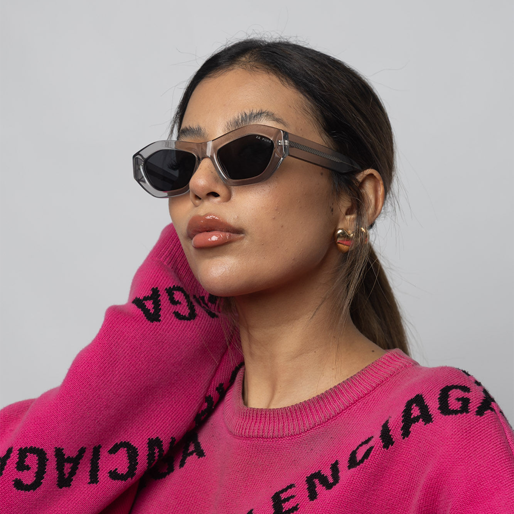 Woman wearing sunglasses and a pink sweater with Balenciaga branding.